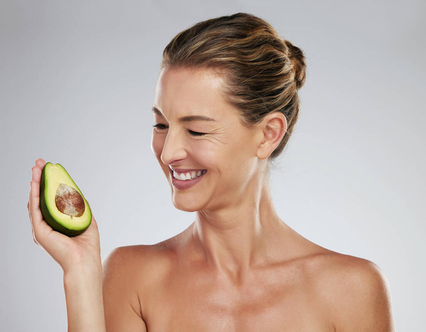Mature woman, happy and avocado in hand for skin health, wellness and face in portrait. Mature model, dermatology and smile with fruit for skincare, anti aging and beauty with natural facial product. - Fotografie, Obrázek