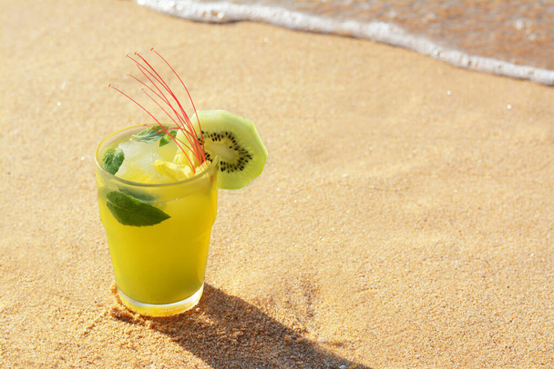 Glass of refreshing drink with kiwi and mint on sand near sea. Space for text - Foto, Imagen