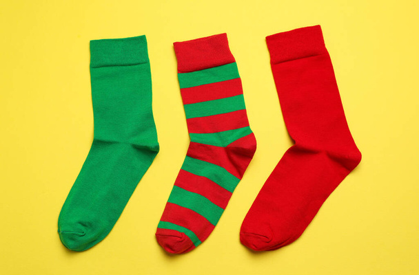 Different green and red socks on yellow background, flat lay - Фото, изображение