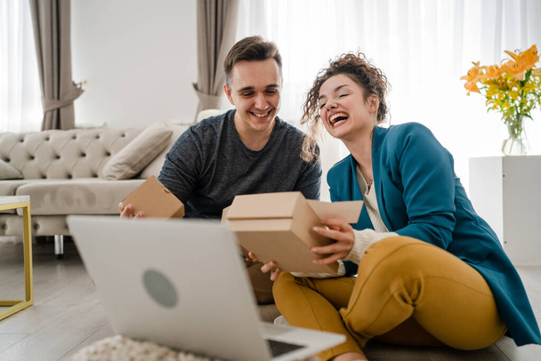 Kafkasyalı genç bir çift, karı-koca, karı-koca ya da erkek arkadaş hediye kutusunu açıyor ve evdeki dizüstü bilgisayarın önünde internetten fotokopi odası arıyor. - Fotoğraf, Görsel