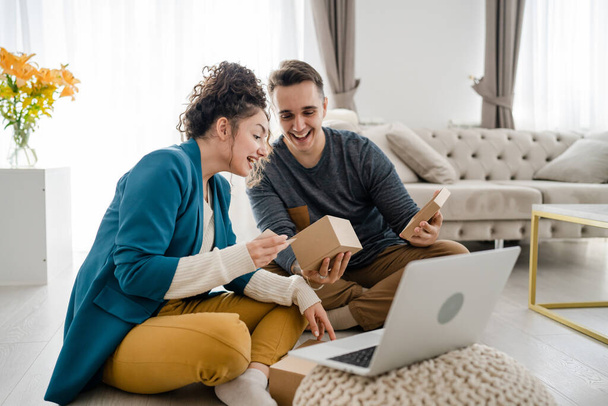 Nuori valkoihoinen pari nainen ja mies vaimo ja aviomies tai tyttöystävä ja poikaystävä avaavat lahjapakkauksen esittelee ja lukee kortin kannettavan tietokoneen edessä kotona, jolla on online-videopuhelukopiotila - Valokuva, kuva