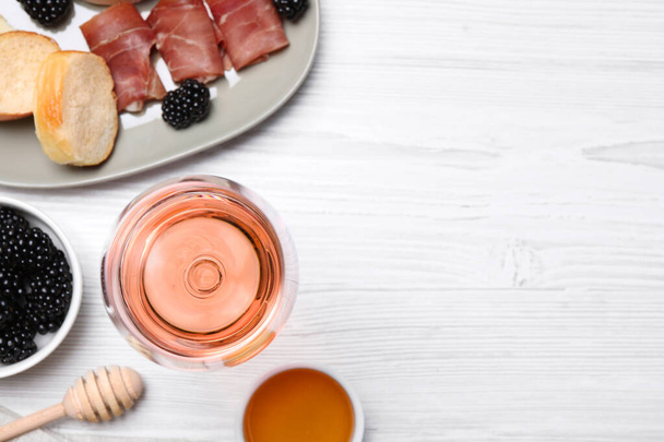 Glass of delicious rose wine and snacks on white wooden table, flat lay. Space for text - Φωτογραφία, εικόνα