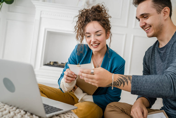 Νεαρή καυκάσια γυναίκα ζευγάρι και ο άνθρωπος γυναίκα και ο σύζυγος ή η φίλη και ο φίλος ανοίγοντας το κουτί δώρων παρουσιάζει και να διαβάσετε την κάρτα μπροστά από τον φορητό υπολογιστή στο σπίτι έχοντας online βιντεοκλήση χαρούμενο χώρο αντίγραφο - Φωτογραφία, εικόνα