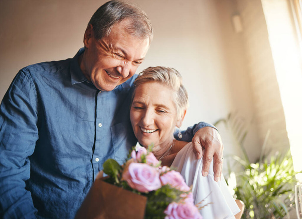 Couple, romance and flowers with a senior man and woman in celebration of valentines day or their anniversary. Retirement, love and affection with an elderly male and female pensioner in their home. - Photo, Image