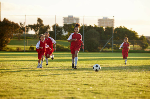 Sports, fitness and soccer training by girl team playing on grass field, teamwork during football game. Health, exercise and children learning to play in competitive match with energy and soccer ball. - 写真・画像