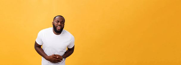 Hombre afroamericano joven usando camiseta blanca con la mano en el estómago porque las náuseas, la enfermedad dolorosa sensación de malestar. Concepto Ache
. - Foto, Imagen