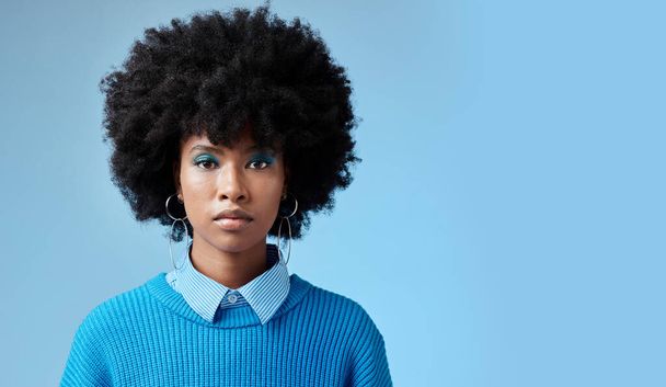 Porträt einer schwarzen Frau, Mode afro und ernstes Gesicht mit einem Ausdruck des Fokus auf blauem Hintergrund Studio-Attrappe. Trendiges Accessoire, stylische coole Kleidung und blaues Kosmetik-Lidschatten-Make-up. - Foto, Bild