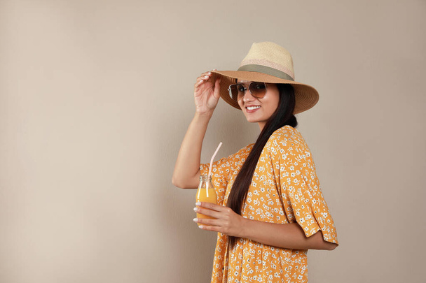 Beautiful young woman with straw hat and glass of refreshing drink on beige background. Space for text - Fotó, kép