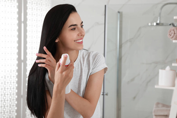 Woman applying dry shampoo onto her hair in bathroom - Foto, imagen