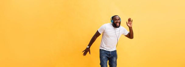 Full length portrait of a cherry young african american man listening to music with headphones and dancing isolated over yellow background. - Foto, Bild