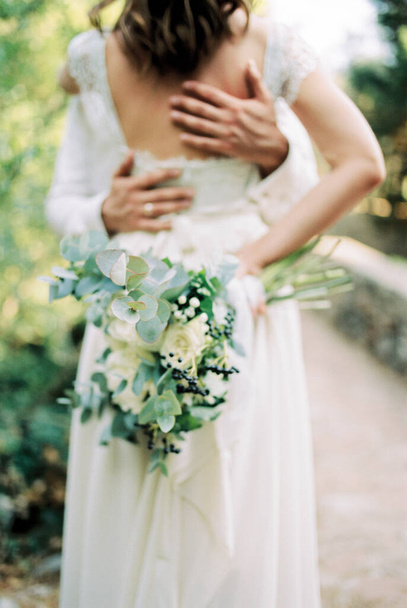 Bräutigam Hände umarmen Braut zurück mit einem Blumenstrauß in der Hand. Beschnitten. Hochwertiges Foto - Foto, Bild