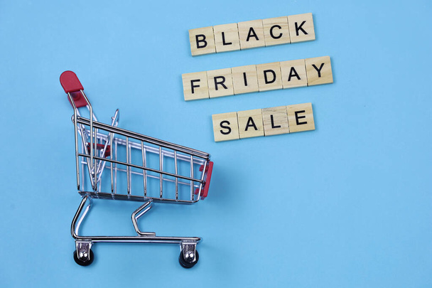 Wooden blocks forming words "black friday sale" and mini shopping cart  isolated on blue background. - 写真・画像