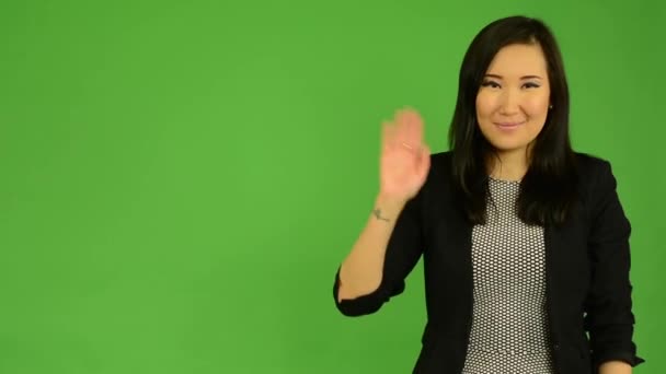 Young attractive asian woman waves with hand - green screen studio - Footage, Video