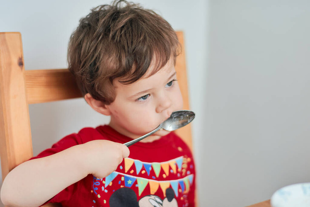 Egy fiú zabkását eszik reggelire a konyhaasztalnál. - Fotó, kép