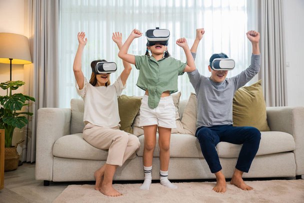 Asian family wear vr glasses headsets sitting on sofa in living room, game entertainment innovation technology, Happy family have mother father and daughter watching movie or playing video game - Fotoğraf, Görsel
