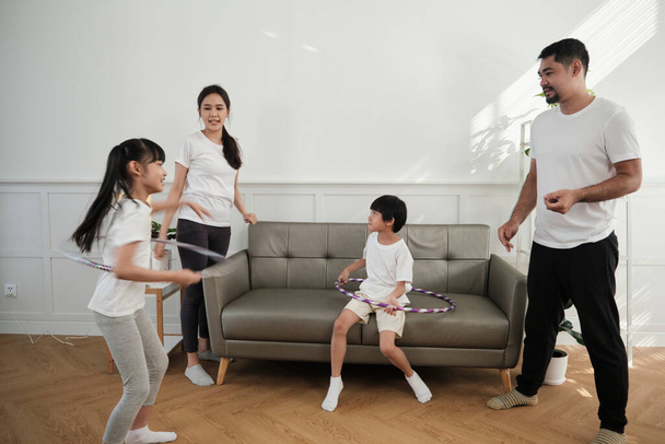 Happy wellness Aziatische Thaise familie, ouders en kinderen zijn leuk spelen hula hoepels samen, fitness training en gezonde oefening in de witte woonkamer, huiselijke levensstijl, en weekend activiteit. - Foto, afbeelding