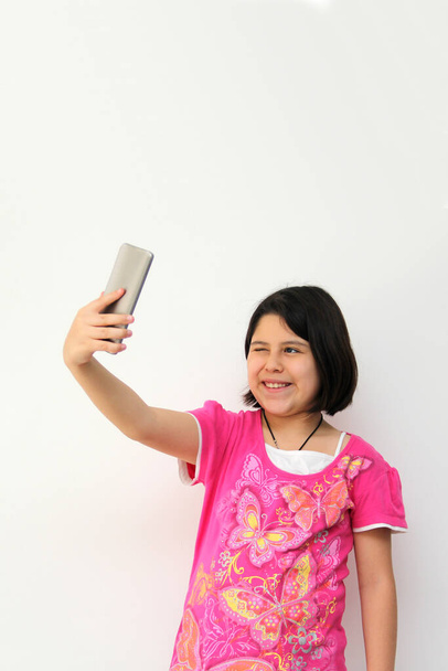 10-year-old Hispanic girl uses her cell phone to make video calls, play video games, send messages, take photos, selfies, watch and record videos as an influencer and have fun in her free time - Fotoğraf, Görsel