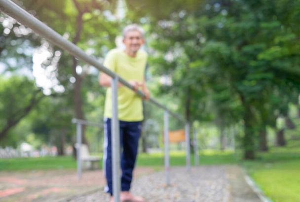 blurred background of senior man with bare feet try to walking himself in rehab equipment at park, concept older adult after chronic illness stroke,paralysis,disability, to be able take care themselves - Fotoğraf, Görsel