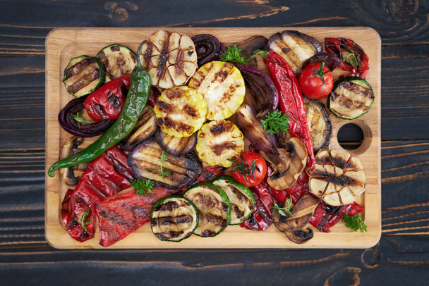 Grilled vegetables mix on a wooden cutting board - zucchini eggplant onions corn mushroom tomato. - Zdjęcie, obraz