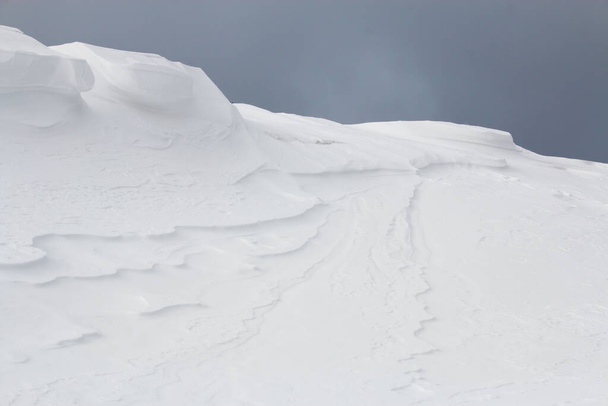 Drifting snow blowing over large white snowdrift - Foto, afbeelding