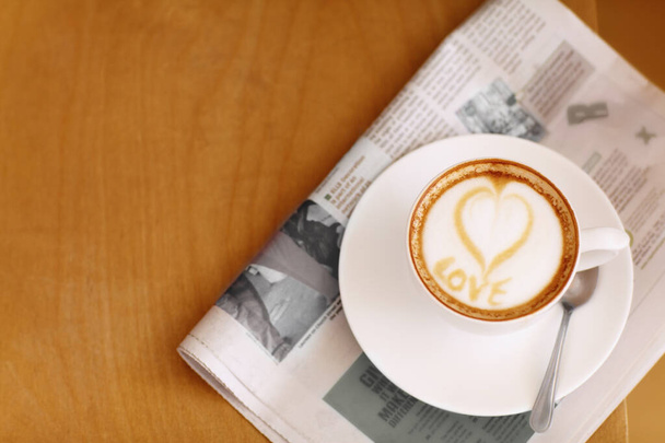 Wykonane z miłości... Wysokie ujęcie z pięknie przygotowanego kubka cappuccino siedzącego na gazecie - Zdjęcie, obraz