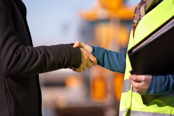 Mimarların inşaatçılarla buluştuğu yerde bir inşaat işçisi mimarla el sıkışıyor. - Fotoğraf, Görsel