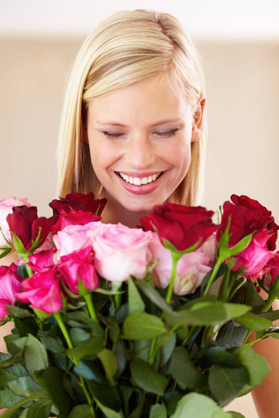 I can smell a hint of vanilla with undertones of musk and jelly beans. A young woman smelling a bouquet of roses - Фото, изображение