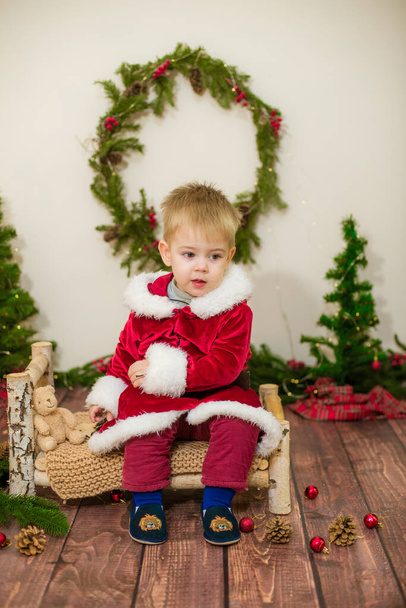 Little cute boy dressed as Santa Claus in a room decorated for Christmas. Christmas and children - Fotó, kép
