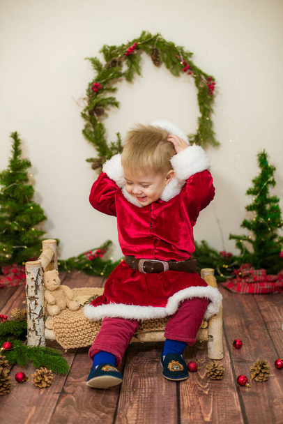 Malý roztomilý chlapec oblečený jako Santa Claus v místnosti zdobené na Vánoce. Vánoce a děti - Fotografie, Obrázek