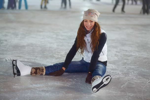 Tanto vale restare quaggiu 'per un po'. Una giovane donna sorridente seduta sul ghiaccio di una pista di pattinaggio - Foto, immagini