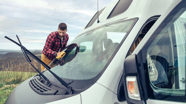 Young man cleaning camper van windshield with cloth outdoor - Photo, Image