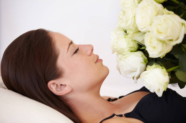 Вдыхает их сладкий запах. Красивая молодая женщина лежит с закрытыми глазами и держа букет белых роз на груди - Фото, изображение