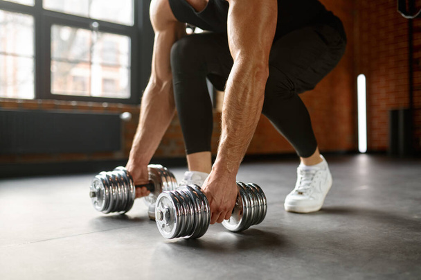 Sportif kolları olan güçlü bir adam spor salonu zemininden dambılları kaldırıyor. Vücut geliştirme konsepti - Fotoğraf, Görsel