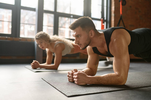 Man and woman stand in plank. Group training at sport club gym class. Focus on sportsman. Fitness workout concept - Photo, Image