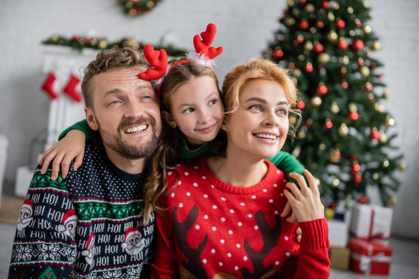 Cheerful kid in christmas headband hugging family at home  - Foto, afbeelding