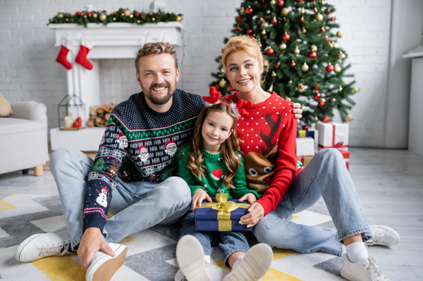 Cheerful family holding gift and looking at camera during christmas at home  - Photo, Image