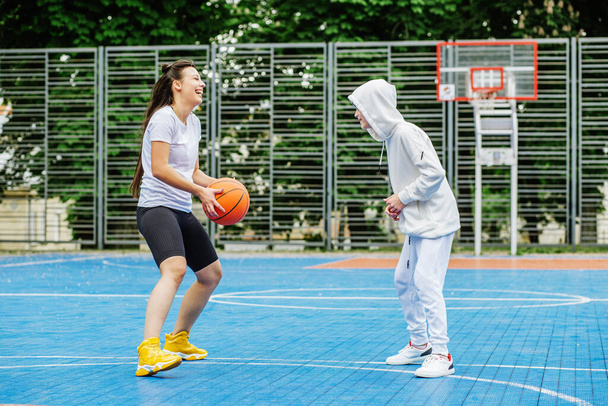 Girl and her younger brother, teenager, play basketball on modern basketball court under open sky. Concept of sports, hobbies and healthy lifestyle. - Valokuva, kuva