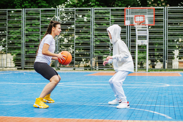 Dziewczyna i jej młodszy brat, nastolatek, grają w kosza na nowoczesnym boisku do koszykówki pod gołym niebem. Pojęcie sportu, hobby i zdrowego stylu życia. - Zdjęcie, obraz