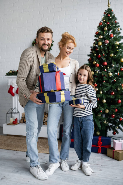 Cheerful family holding gifts near decorated christmas tree in living room  - Foto, Imagem
