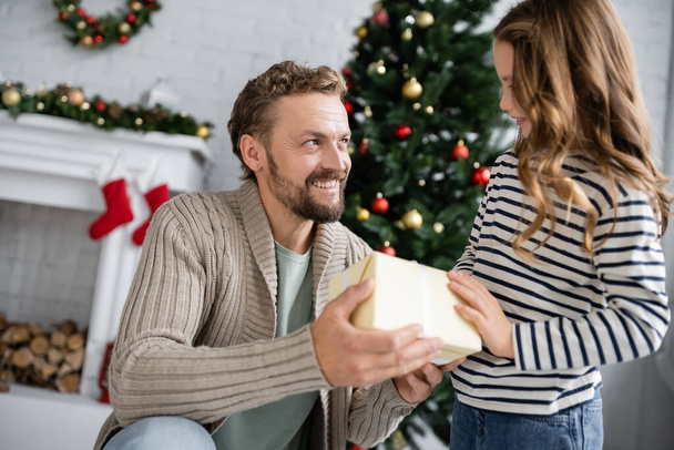 Positive dad in knitted cardigan giving present to daughter during christmas at home  - Photo, image