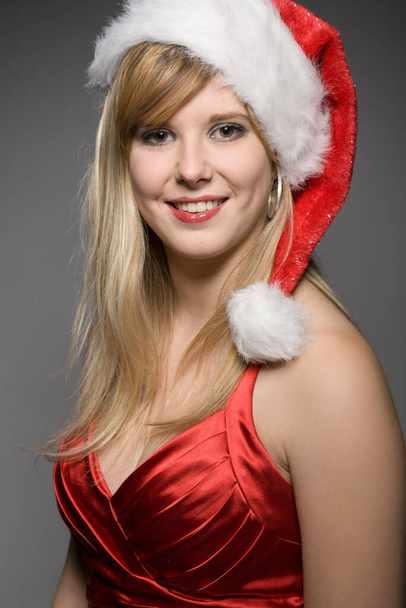 mooie kerst meisje met kerstman hoed in de voorkant van een grijze achtergrond - Foto, afbeelding