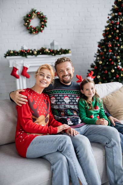 Man in warm sweater hugging daughter and wife on couch at home  - Photo, Image