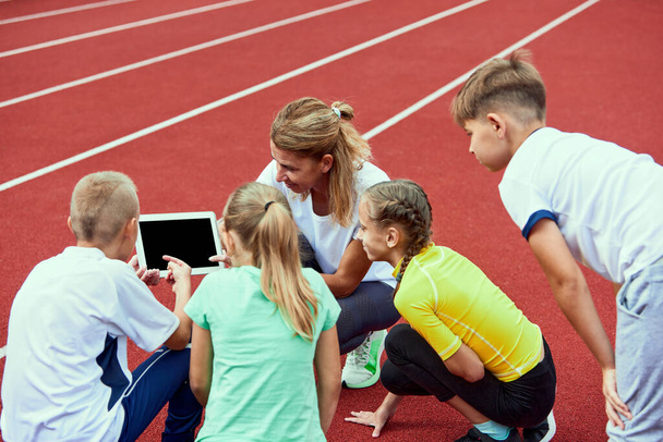 Team work, result strategy. Female coach training athletes. Group of children before running on treadmill at the stadium. Concept of sport, achievements, studying. Method of work and training. - Photo, image