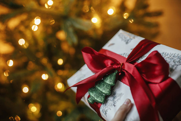 メリークリスマスとハッピーホリデー!黄金の光とクリスマスツリーでスタイリッシュなクリスマスプレゼント。夜の部屋で赤い弓と光沢のある木の装飾が施されたクリスマスプレゼントを包んだ。大気旗 - 写真・画像