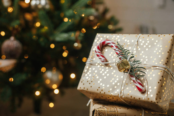 Cadeaux de Noël élégants à l'arbre de Noël avec des lumières dorées. Cadeaux de Noël enveloppés avec canne à bonbons sous arbre décoré dans la chambre. Joyeux Noël et Joyeuses Fêtes ! Bannière atmosphérique - Photo, image
