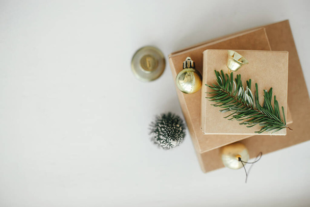 Buon Natale! Elegante eco scatole regalo di Natale sulla tavola bianca posa piatta. Semplici regali di Natale artigianali con bagattelle d'oro, campana e ramo di abete su legno rustico. Zero sprechi. Spazio per testo - Foto, immagini