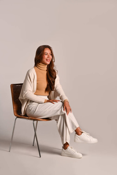 Полный портрет красивой женщины в тёплом свитере, сидящей на стуле на белом фоне. Снимок студии. - Фото, изображение