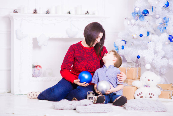 A young mother with dark hair with her son near a white Christmas tree  in a room decorated for Christmas. Family Christmas. Christmas mood - Φωτογραφία, εικόνα
