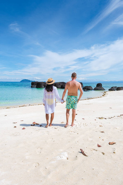Hombres y mujeres en pantalones cortos de baño caminando en una playa tropical blanca en Tailandia, Koh Kham Trat. hombres en nadar corto y mujeres asiáticas en la playa con palmeras y arena blanca - Foto, imagen