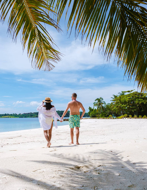 Men and women in swim shorts walking on a white tropical beach in Thailand, Koh Kham Trat. men in swim short and Asian women on the beach with palm trees and white sand - Photo, Image
